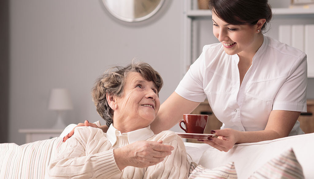 A Hospice Caregiver Handing a Mug to a Senior Woman Sitting on a Couch Benefits of Non-profit Hospice